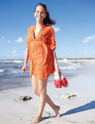 Woman carrying a pair of sandals while walking on the beach.