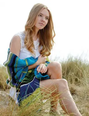 Woman sitting in a grassy area wearing a crocheted stole.