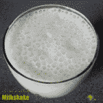 Banana Milkshake Recipe shown in a glass with lots of bubbles on top.