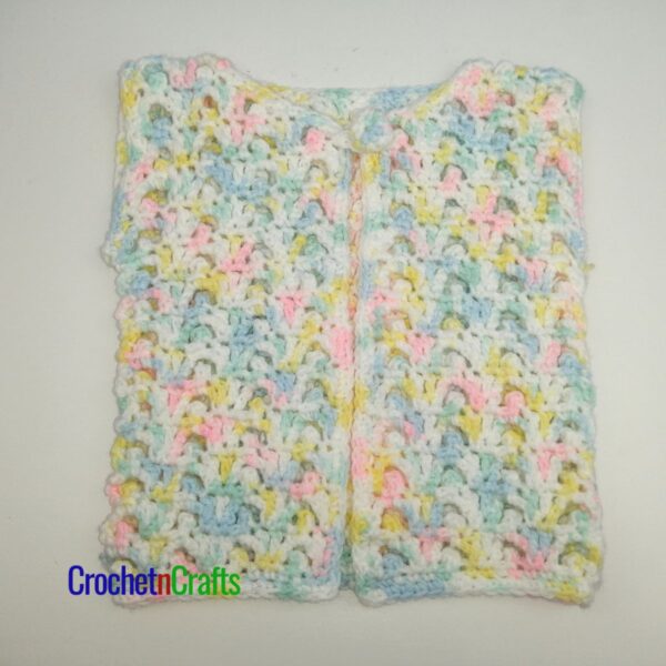 A crochet baby vest is laid flat.