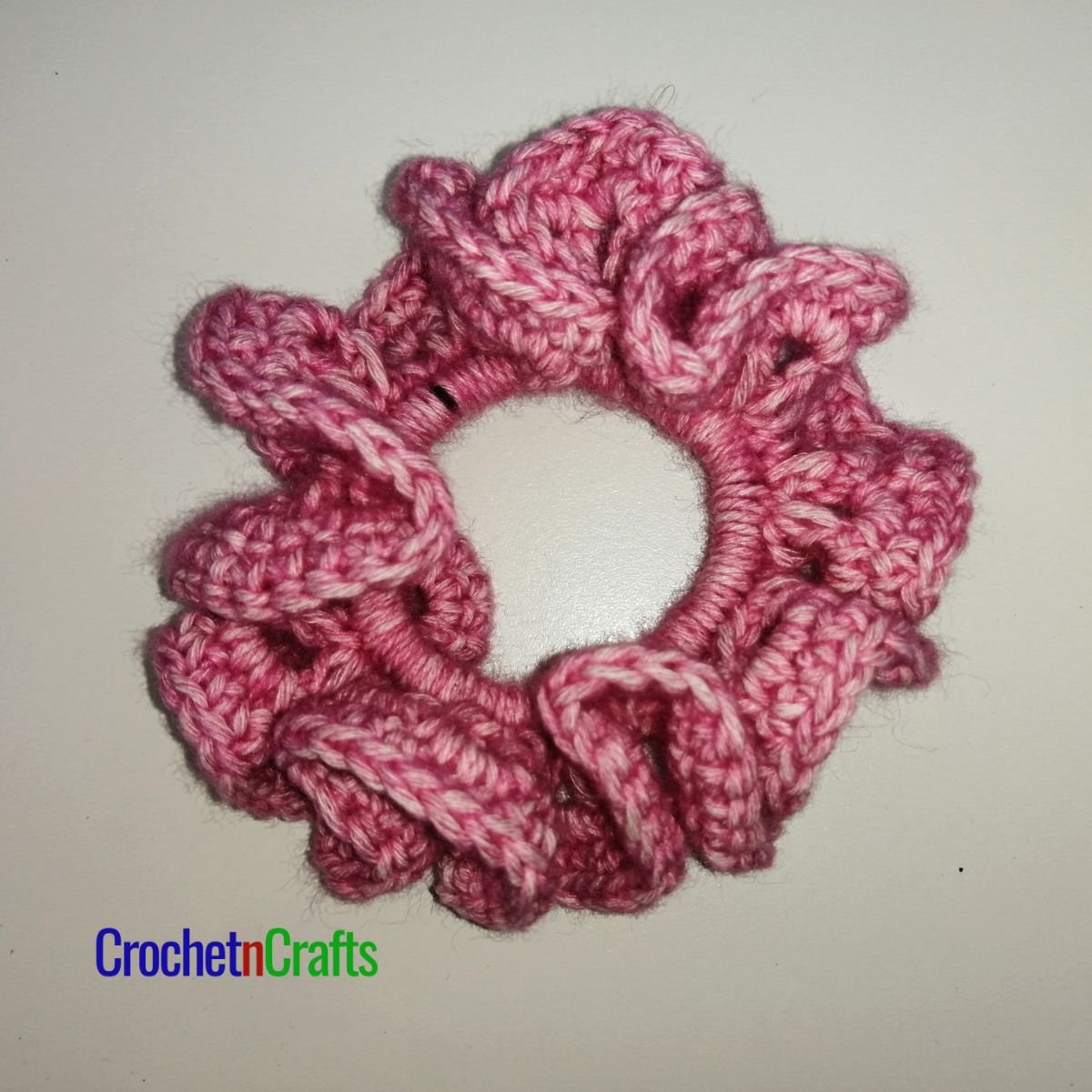 Crochet hair scrunchie shown in pink yarn called Stonewashed by Scheepjes.