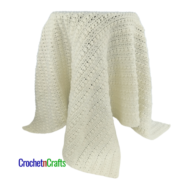 Textured crochet baby blanket shown in white - draped over a stool.