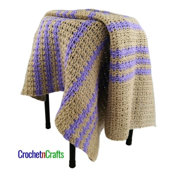 A crocheted baby blanket draped over a stool.