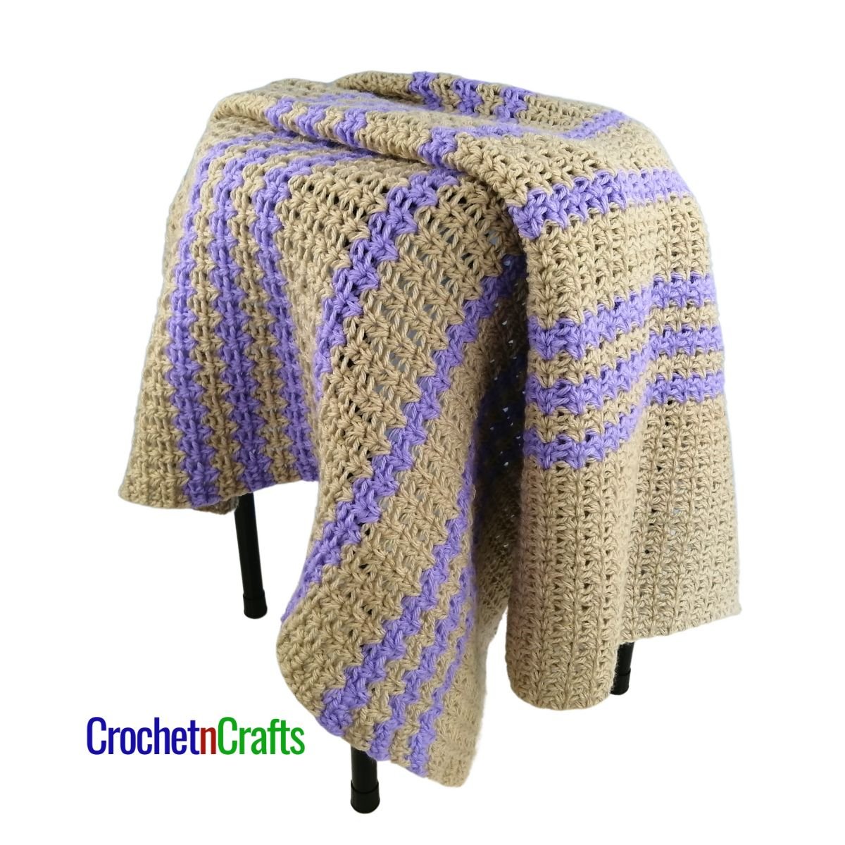 A crocheted baby blanket -draped over a stool.