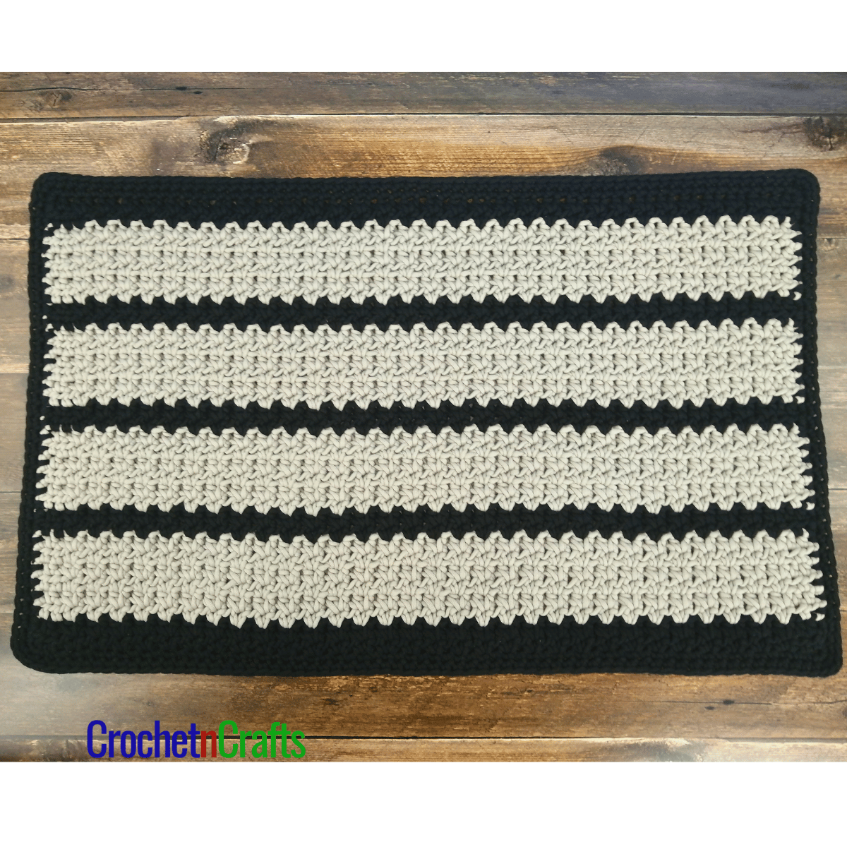 A rectangular crochet floor mat shown on a wooden floor.