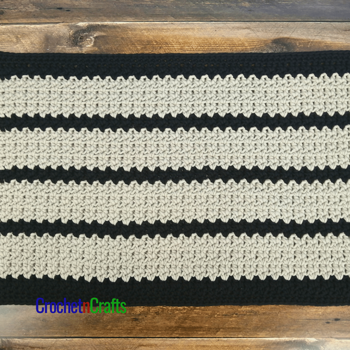 A crocheted floor mat shown on a wooden floor.