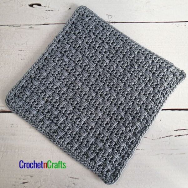 A crocheted dishcloth worked up in the horizontal puff stitch using Lion Brand 24/7 Cotton yarn.