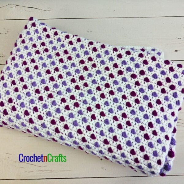 A colorful blanket folded up, showing one side of the ball stitch.